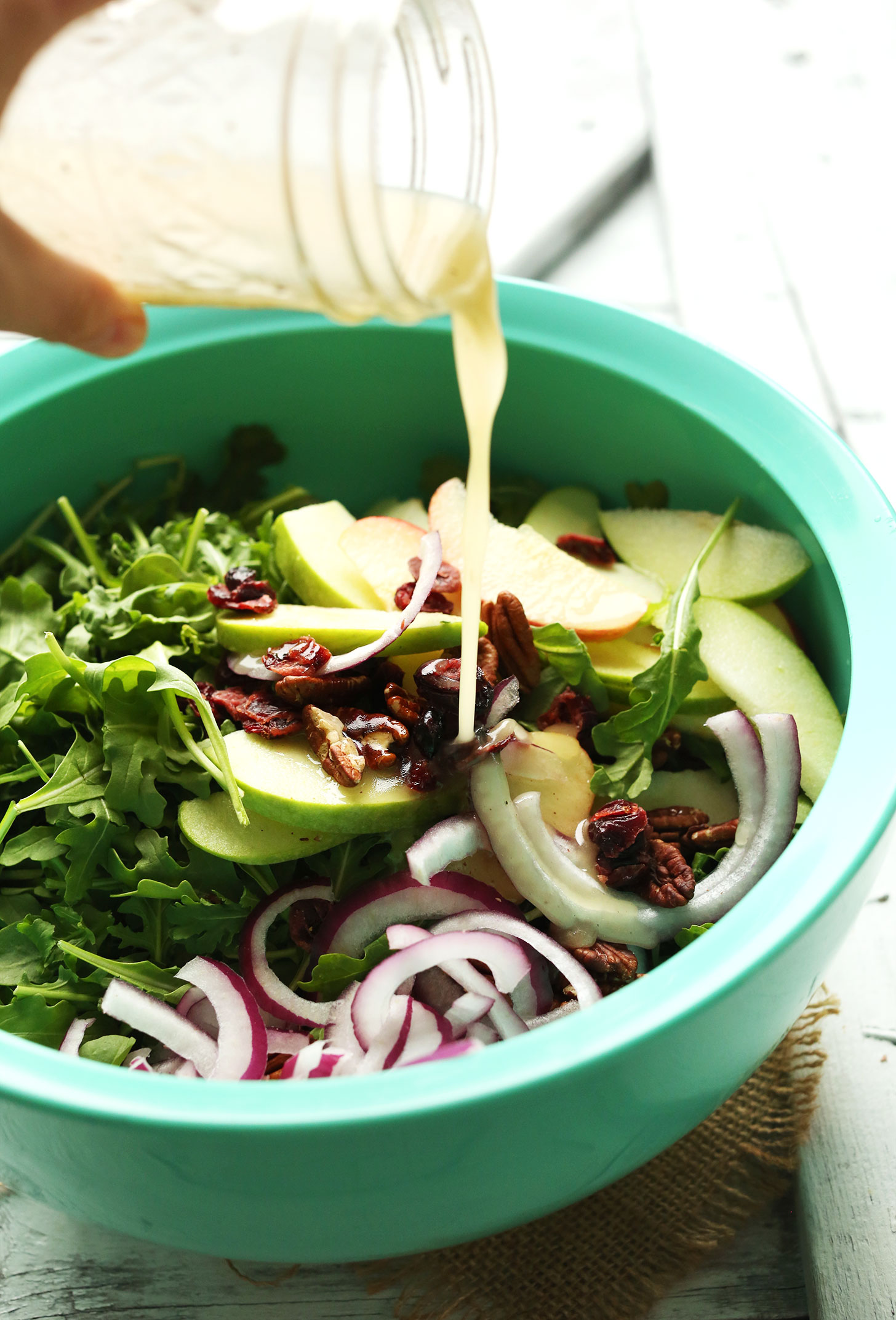 Pouring delicious homemade lemon vinaigrette onto our Easy Apple Arugula Salad with Pecans