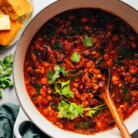 Hands holding the handles of a Dutch oven of pumpkin turkey chili