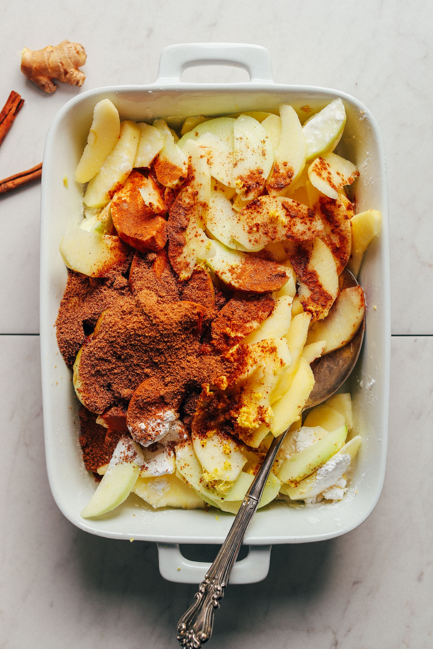 Ceramic baking dish with freshly sliced apples and spices for making our Cinnamon Baked Apples recipe