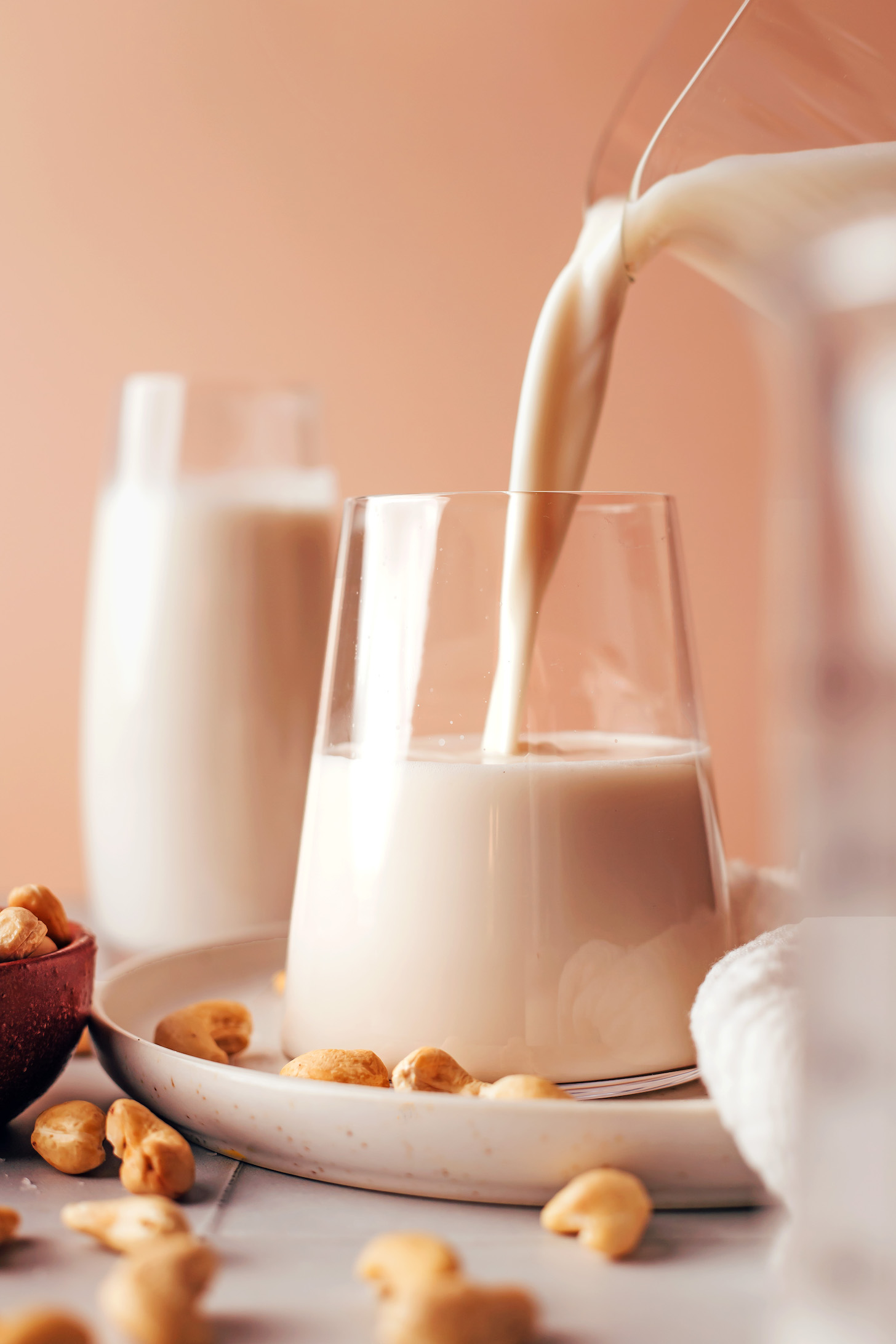 Pouring homemade cashew milk from a pitcher into a glass