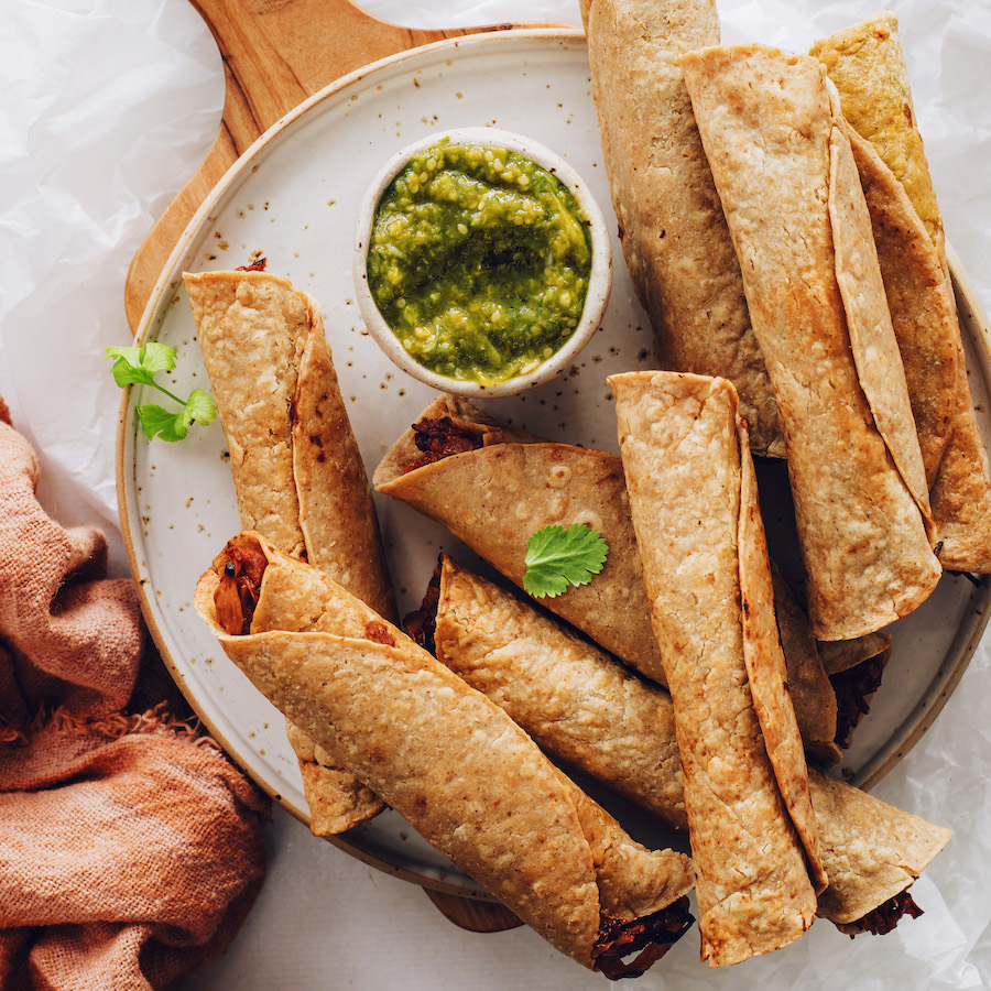 Jackfruit taquitos on a plate around a bowl of green salsa