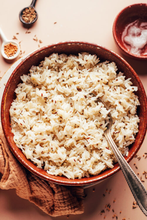 Spoon in a bowl of fluffy jeera rice with spices around it