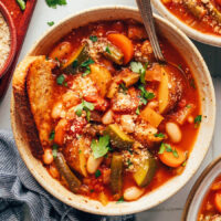 Overhead photo of a bowl of veggie white bean minestrone served with a slice of bread