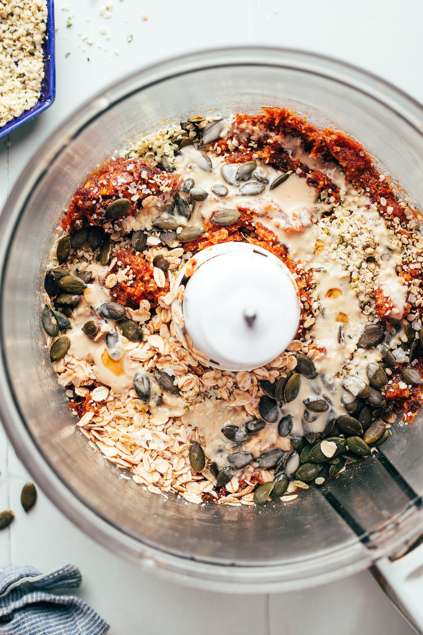 Food processor with blended dates, rolled oats, pumpkin seeds, hemp seeds, tahini, and sea salt