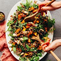 Using salad tongs to grab a scoop of Roasted Squash Salad with Nut Cheese and Balsamic Reduction