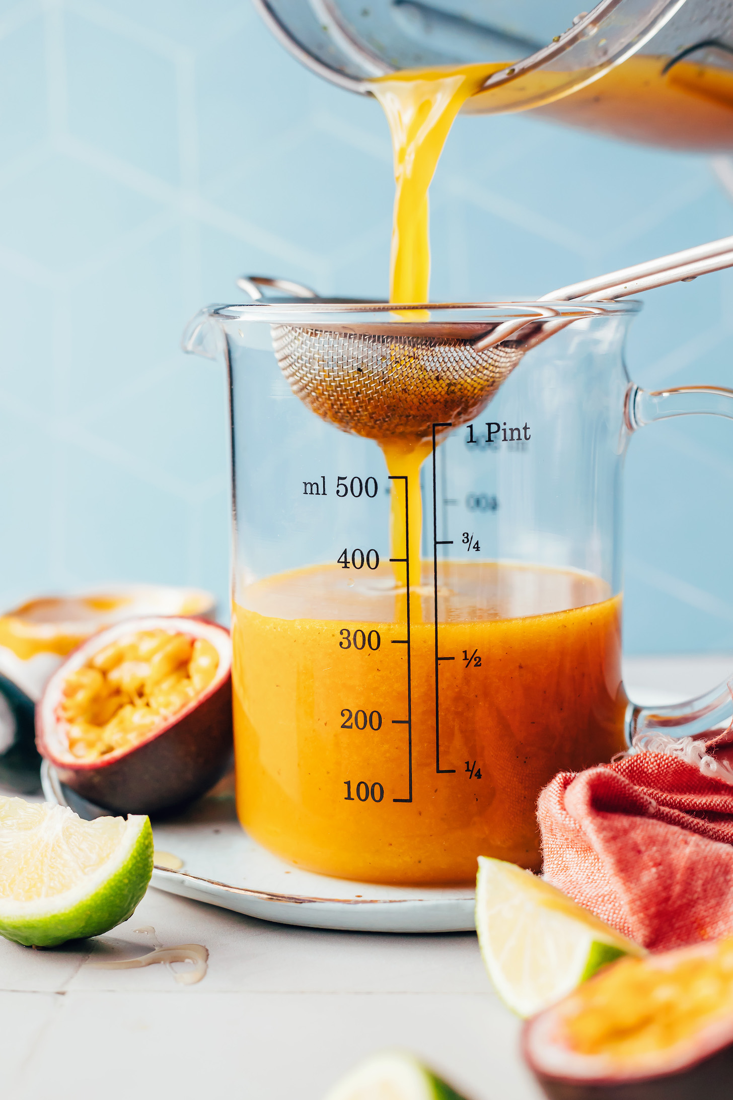 Pouring the passion fruit mocktail mixture through a strainer to remove the jalapeño skin