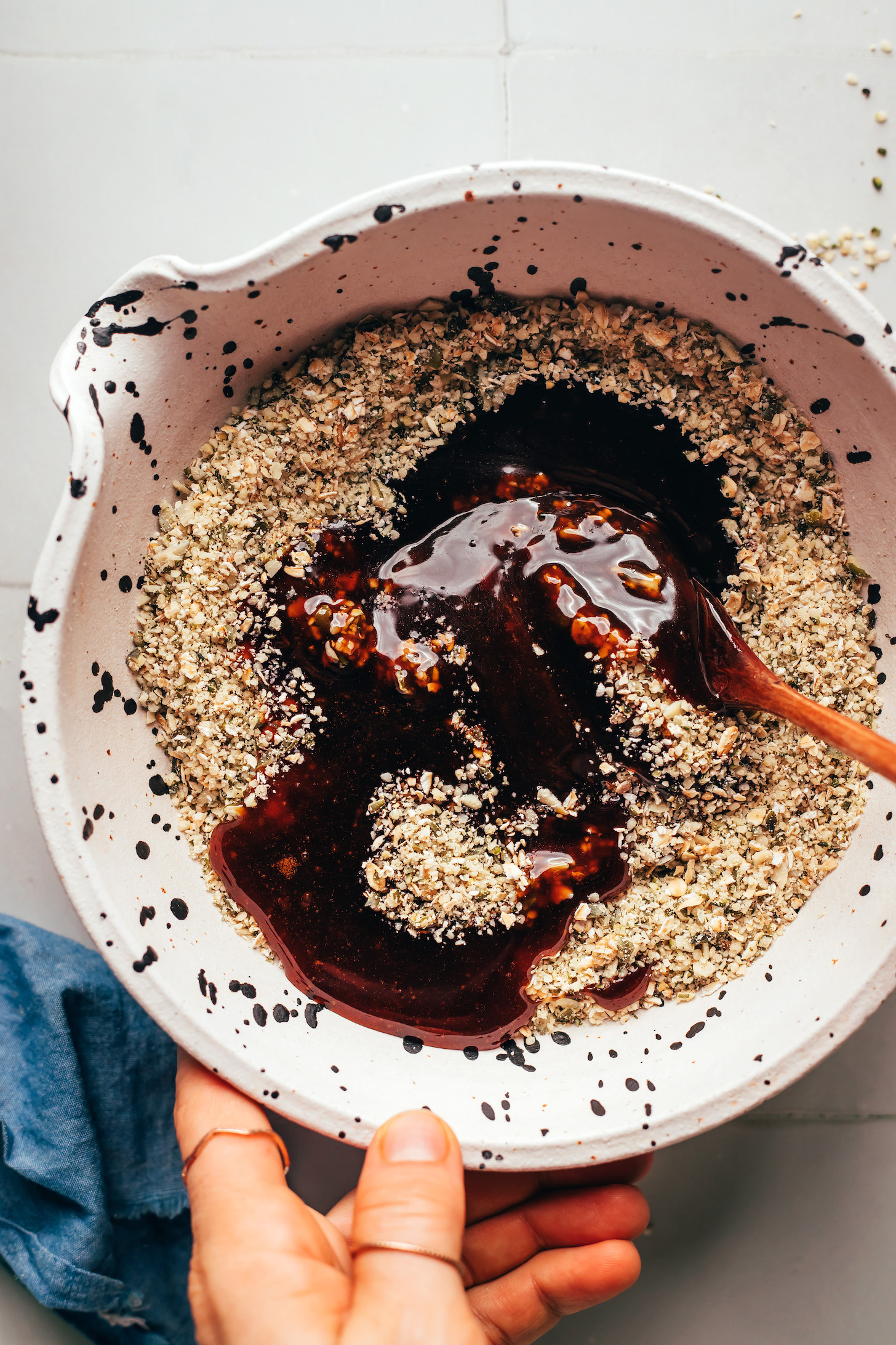 Using a wooden spoon to mix together an oat and seed meal with a naturally sweetened caramelly sauce