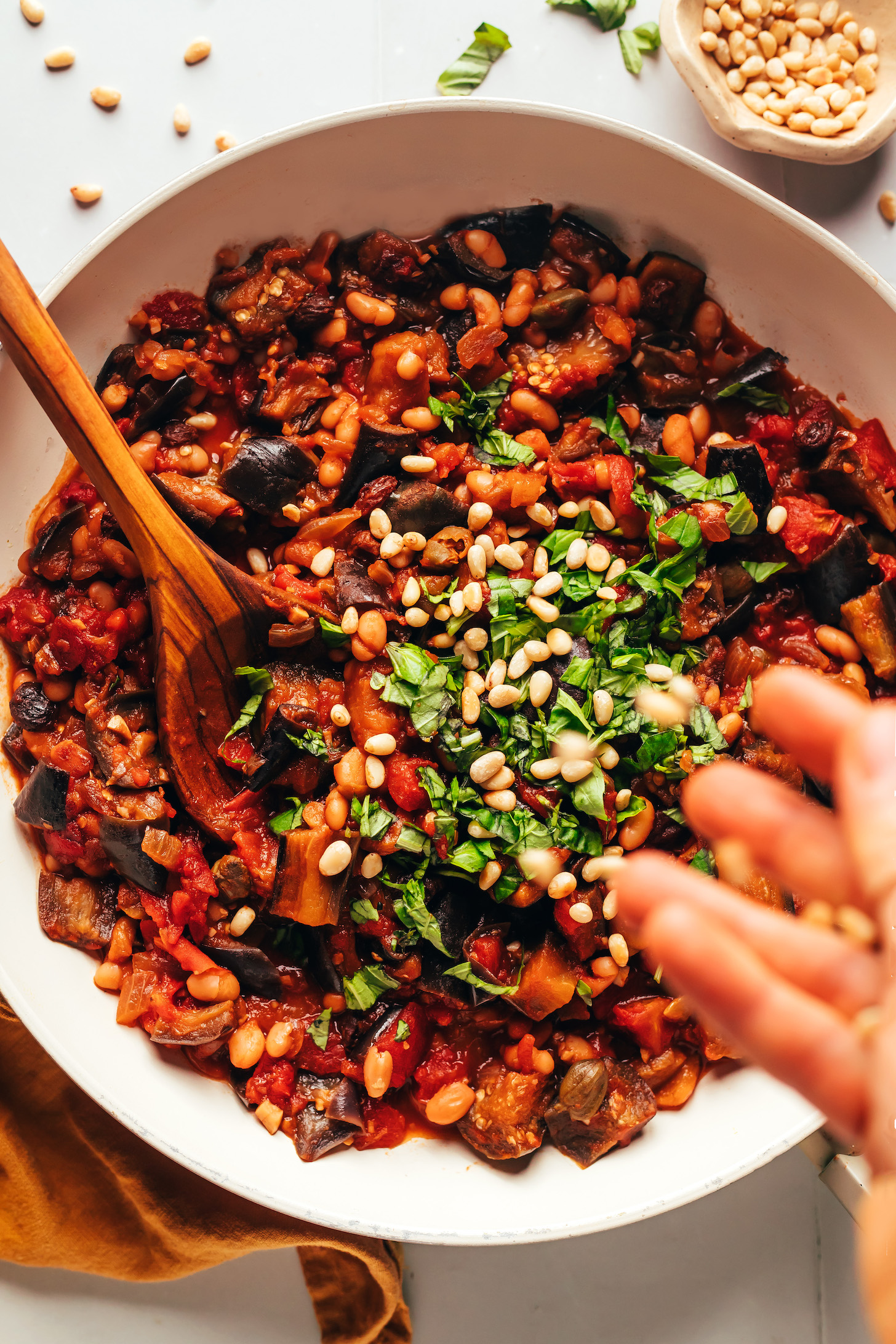 Adding toasted pine nuts into a skillet of white bean eggplant caponata